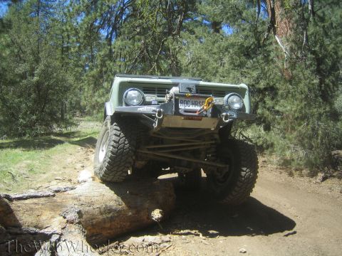 1987 Suzuki Samurai - Off-road vehicle navigates a challenging trail, crossing over a large fallen tree on a sunny day.