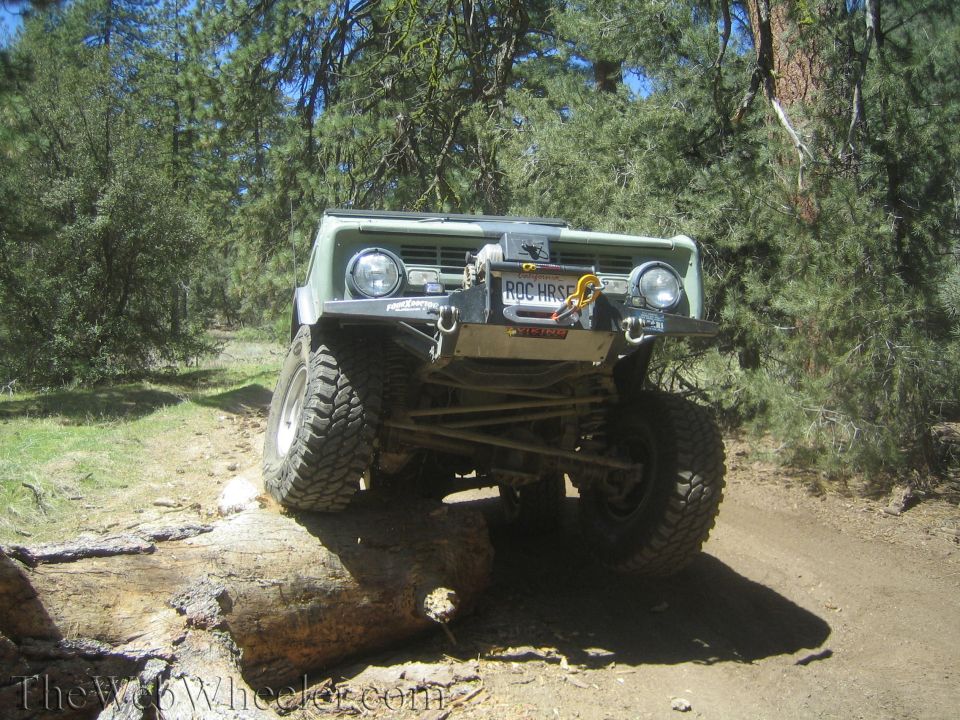 Off-road vehicle with large tires driving over a fallen tree on a dirt path. License plate reads ROC HRSE