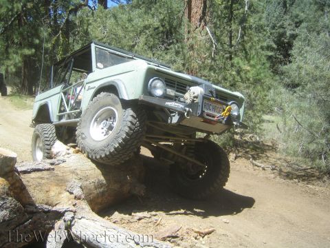 1987 Suzuki Samurai - This modified Ford Bronco is navigating a challenging off-road obstacle on a sunny day.
