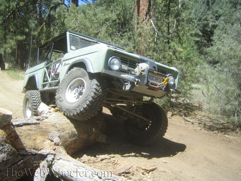 Off-road Bronco climbing over a log on a dirt trail