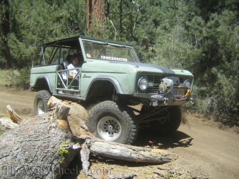 1987 Suzuki Samurai - A modified Ford Bronco navigates a rough trail, climbing over a large log.