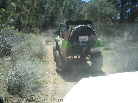 1987 Suzuki Samurai - Two off-road vehicles navigate a dusty trail through a wooded area.