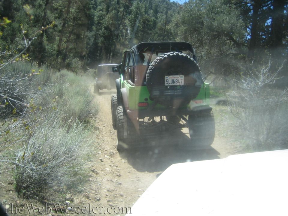 Green off-road vehicle with spare tire on back, driving on a dirt road