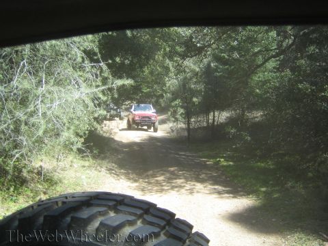 1987 Suzuki Samurai - Two off-road vehicles navigate a dirt path surrounded by trees. The photo is taken from another vehicle.