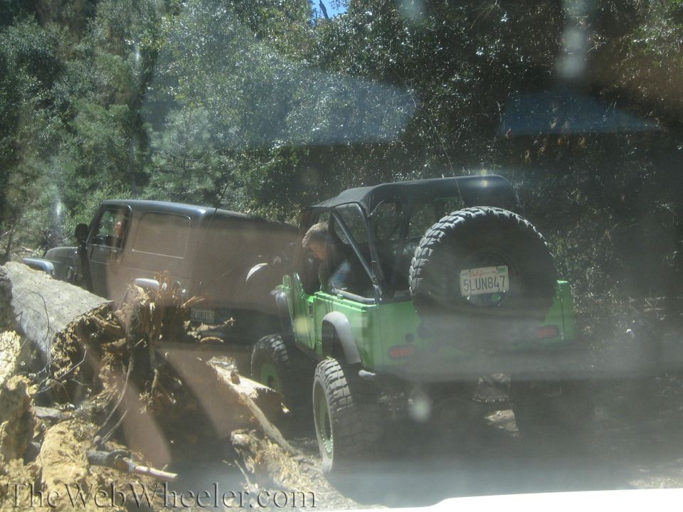 Green Jeep with spare tire on rear, off-roading with another vehicle