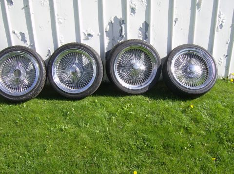 1996 Ford Probe - Four chrome wire wheels with tires are displayed outdoors against a white wall.