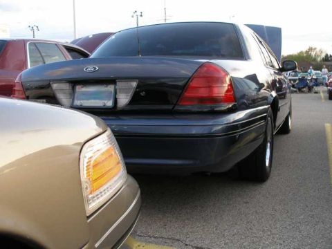 1998 Ford Crown Victoria - A dark blue 1998 Ford Crown Victoria is parked at an outdoor car show, with its hood open.
