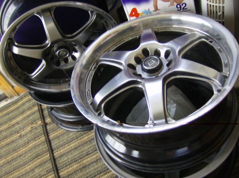 1996 Ford Probe - A stack of shiny alloy wheels, some with a polished lip and five spokes, are displayed indoors.