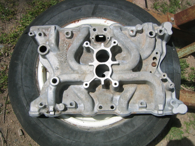 Aluminum V8 intake manifold resting on a tire and wheel outdoors
