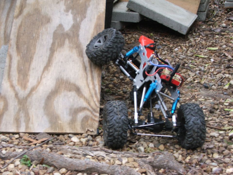 Remote control rock crawler with blue shocks climbing over wood