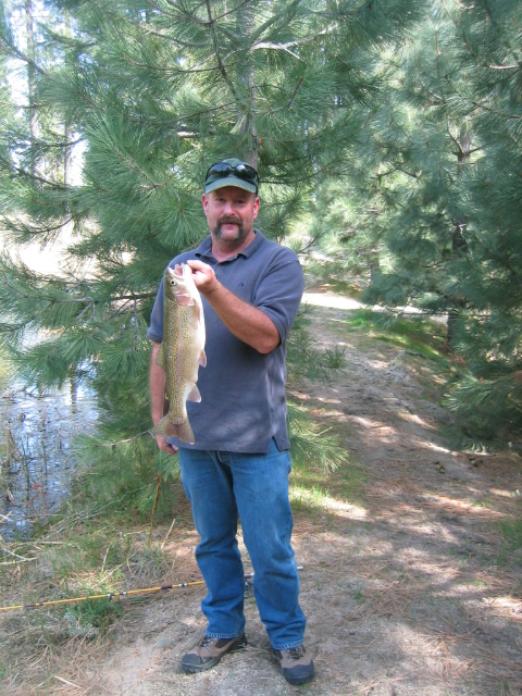 1973 Ford F-100 - A man proudly displays a freshly caught trout while standing near a body of water and pine trees.