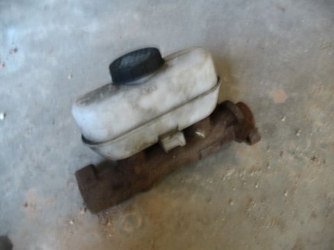 1989 Ford Bronco - A brake master cylinder reservoir with its cap sits on a rusty metal component.