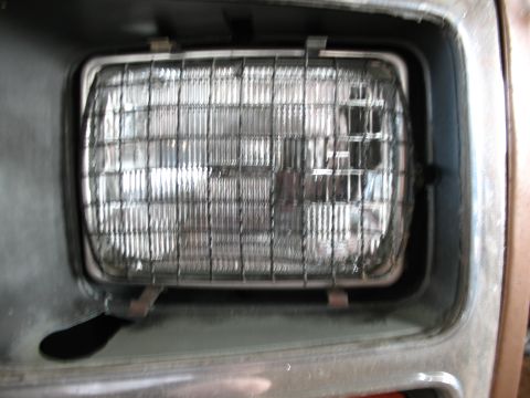 1989 Ford Bronco - Close-up of a vehicle headlight assembly with a protective wire grille. The 'SUPERMOTORS.NET' watermark is visible.
