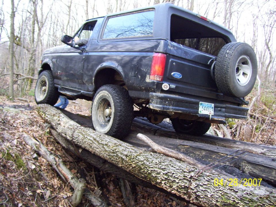 Dark blue Ford Bronco crawling over logs on a wooded trail