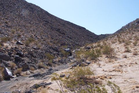 1990 Ford Bronco - A lone off-road vehicle navigates a desert wash, surrounded by sparse vegetation and rocky terrain.
