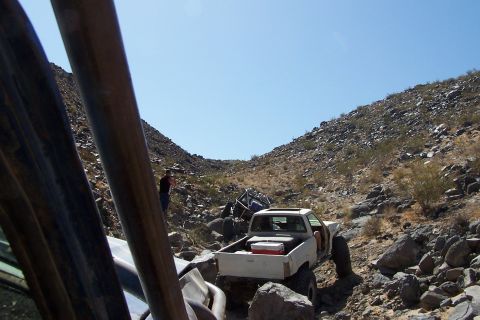 1990 Ford Bronco - A white pickup truck navigates a rocky off-road trail, with another vehicle visible further up the path.