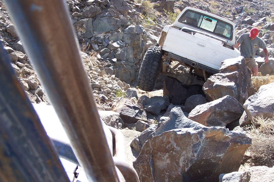 White pickup truck with large tires climbing over rocks, viewed from another vehicle
