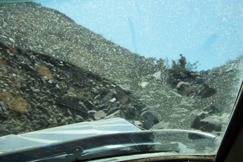 1990 Ford Bronco - The view from inside a vehicle shows a dusty windshield looking out onto a rocky, off-road landscape with a person visible in the distance.
