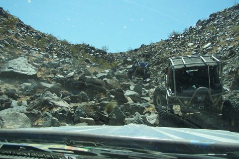 1990 Ford Bronco - Two custom off-road buggies navigate a steep, rocky incline under a clear blue sky.