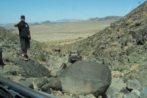 1990 Ford Bronco - A person watches an off-road vehicle descend a challenging rocky trail in a desert environment.