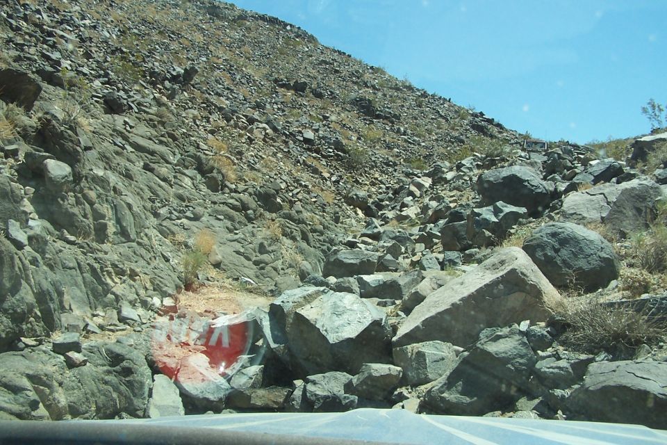 Red and white sign partially obscured by rocks on a rocky hillside