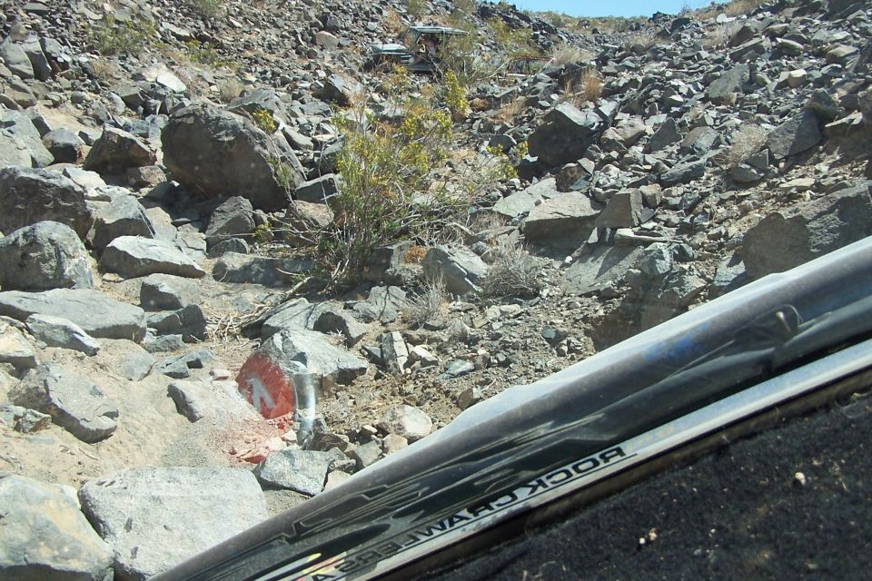 View from inside an off-road vehicle looking out at a rocky trail with other vehicles in the distance