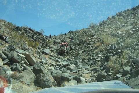 1990 Ford Bronco - An off-road vehicle navigates a steep, rocky terrain under a clear blue sky.