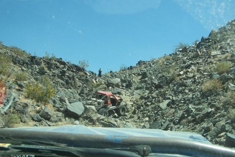 1990 Ford Bronco - A heavily modified red off-road vehicle tackles a challenging rocky terrain, demonstrating its off-road capabilities.