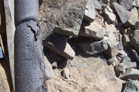1990 Ford Bronco - The insulation on this pipe appears to be cracked and worn, set against a backdrop of rough, natural rocks.