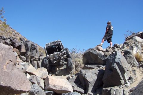 1990 Ford Bronco - A modified off-road vehicle navigates a steep, rocky incline under a clear blue sky.