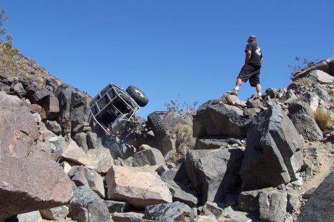 1990 Ford Bronco - Off-road buggy tipped on its side in rocky terrain, a person watches from above.