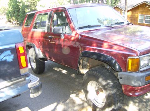 1986 Ford Bronco - A maroon SUV is parked next to a blue pickup truck in a driveway.