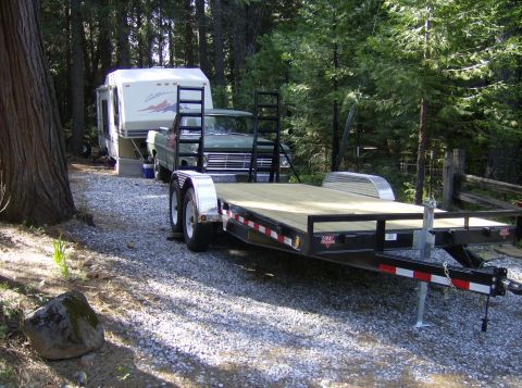1986 Ford Bronco - A green pickup truck is parked next to a camper trailer and a flatbed trailer.