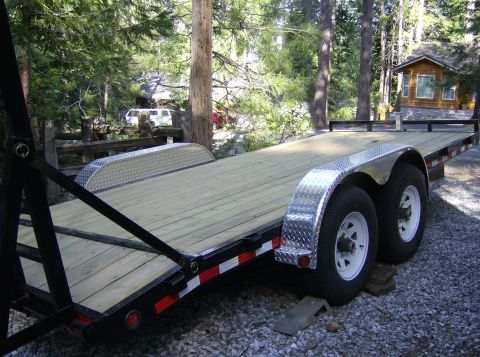 1986 Ford Bronco - A car trailer sits on a gravel lot surrounded by trees, with a cabin visible in the background.