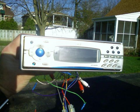 1993 Ford Bronco - A car stereo unit with its wiring harness is held up for inspection against a residential background.