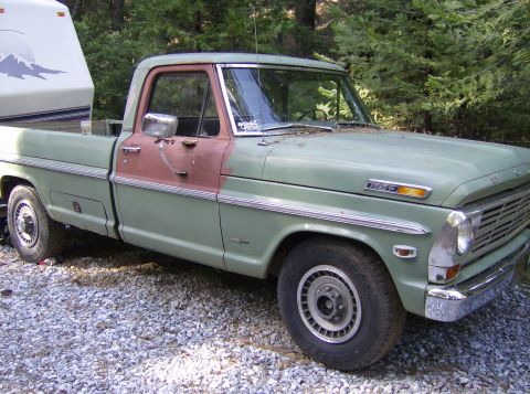 1986 Ford Bronco - This vintage Ford pickup truck is equipped with a camper shell in its bed, parked on a gravel surface.