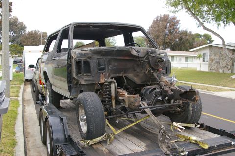 1986 Ford Bronco - A heavily damaged Ford Bronco is transported on a trailer, its front end stripped bare.