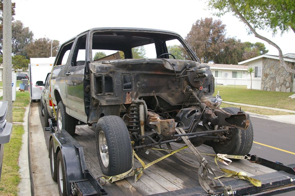 Demolished Ford Bronco on a trailer, front end removed, dark exterior