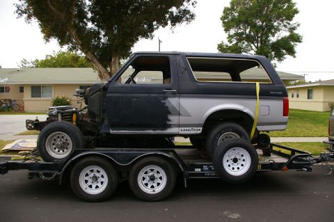 1986 Ford Bronco - A black and silver Ford Bronco is loaded onto a trailer, with its front end disassembled.