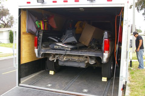 1986 Ford Bronco - A pickup truck bed is filled with various parts and items while parked inside a trailer.
