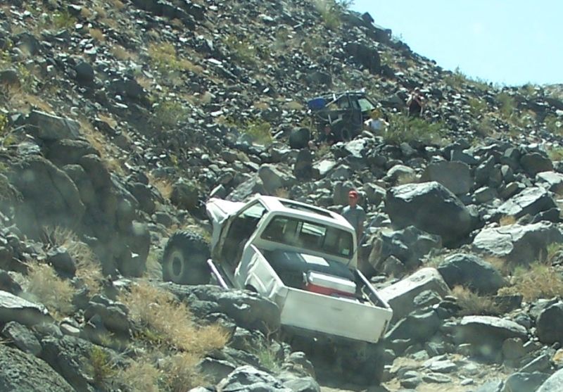 White pickup truck with open doors and sunroof navigating a rocky, off-road trail
