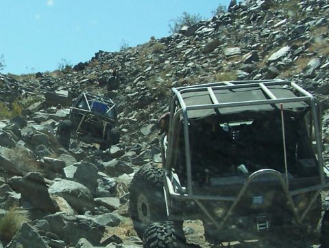 1990 Ford Bronco - Custom off-road vehicles tackle a challenging rocky trail in a desert landscape.