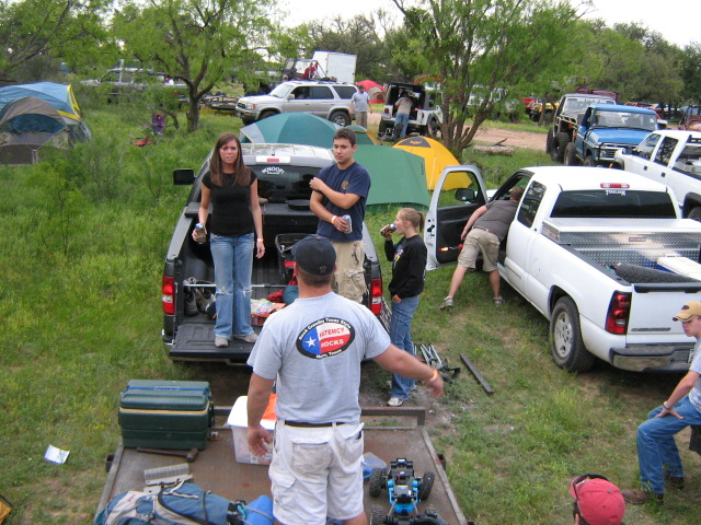 Off-road event campsite with dark pickup, white Silverado, tents and people in a grass field