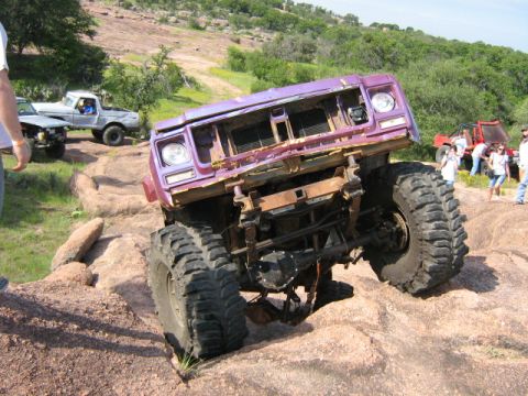 1986 Ford Bronco - This heavily modified SUV is tackling a challenging off-road course with other vehicles and spectators present.