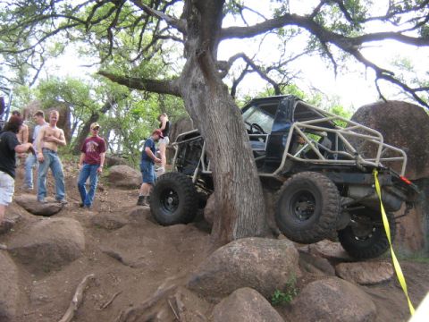 1986 Ford Bronco - A heavily modified off-road vehicle with a prominent roll cage is shown maneuvering through a challenging rocky landscape.