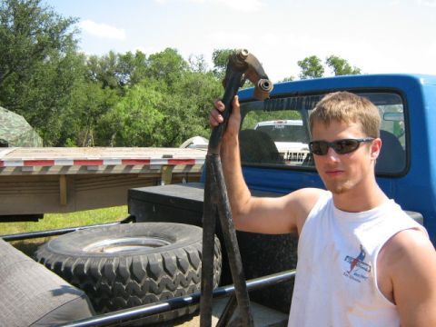 1986 Ford Bronco - Man holds a suspension part, with a blue truck and trailer in the background.