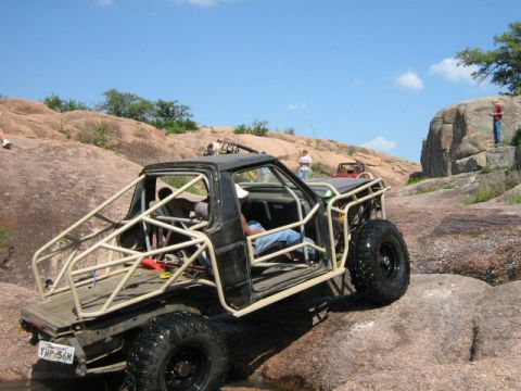 1986 Ford Bronco - Modified off-road truck navigates rocky terrain with a prominent roll cage.