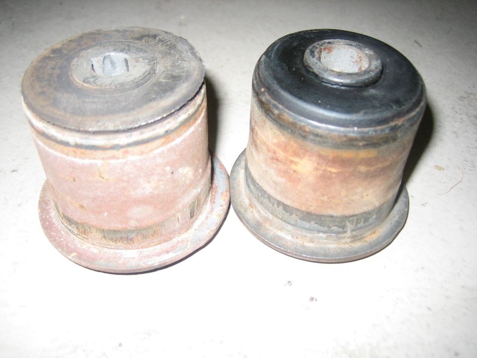 Two rusty bushings, one with a black rubber top, on a white surface