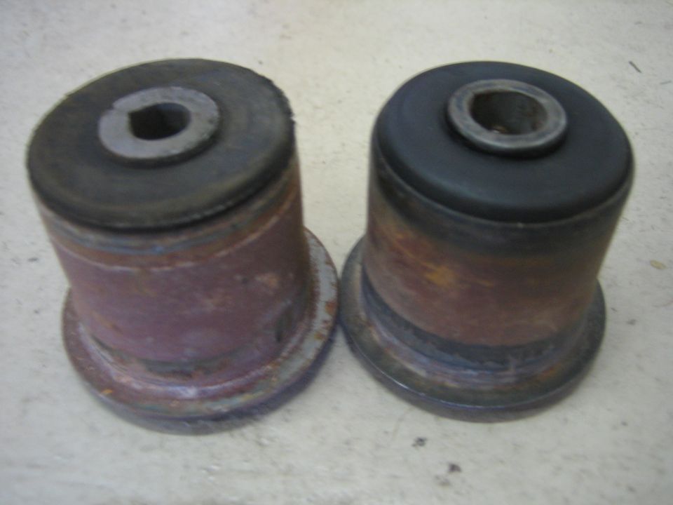 Two used suspension bushings, one with a black rubber top and the other with a worn metal top
