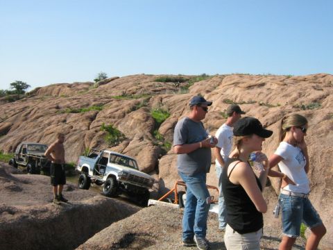 1986 Ford Bronco - Off-road enthusiasts tackle challenging terrain with their modified vehicles under a clear blue sky.